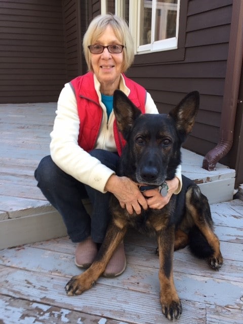 Adele sitting on a step arms around dark sable fidelco pup feebee sitting at her feet