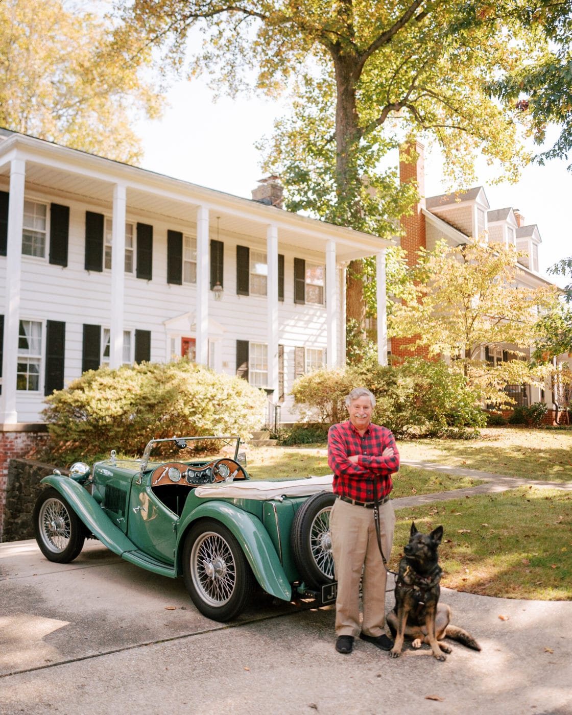 fidelco client steve smiling with his guide dog cricket sitting by his feet in front of his vintage car