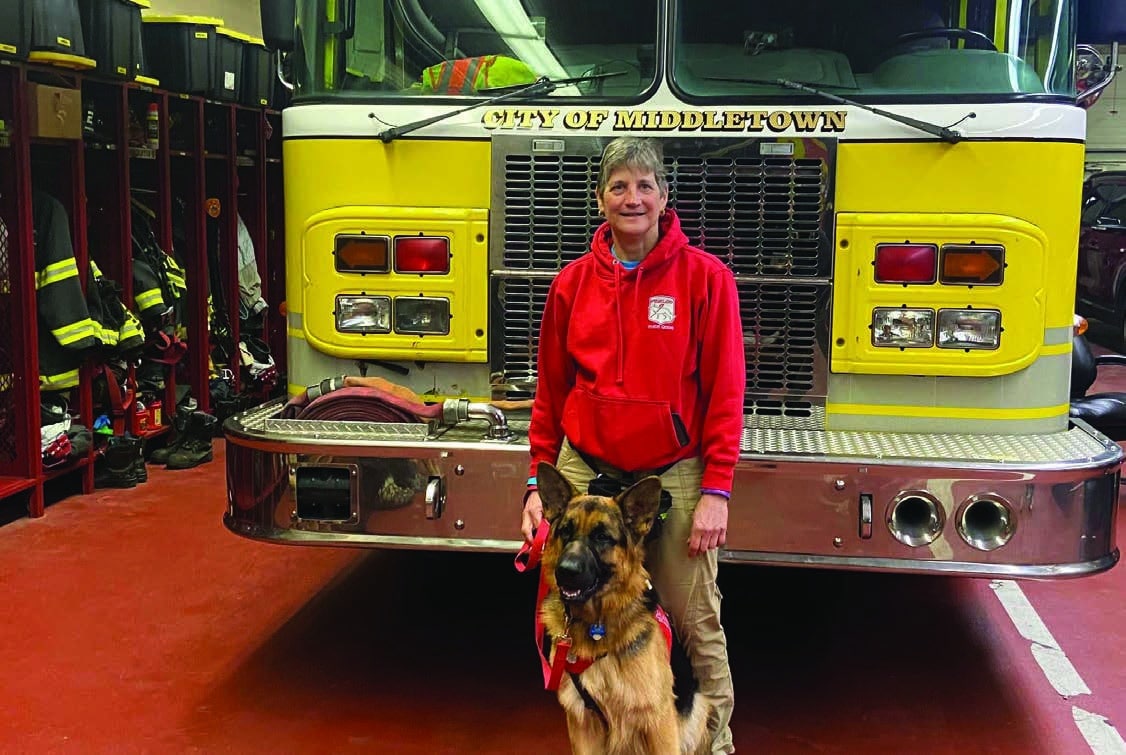 Kim standing in front of fire truck with Hagrid between her legs.