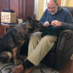 Todd sitting in a chair holding an item that fergus is inspecting carefully