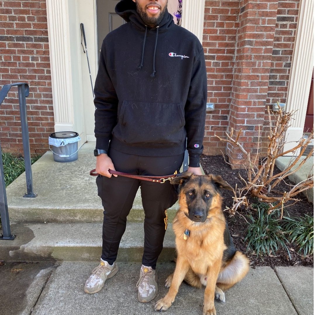 quinn standing holding yuri's lead on the sidewalk in front of the door to a building